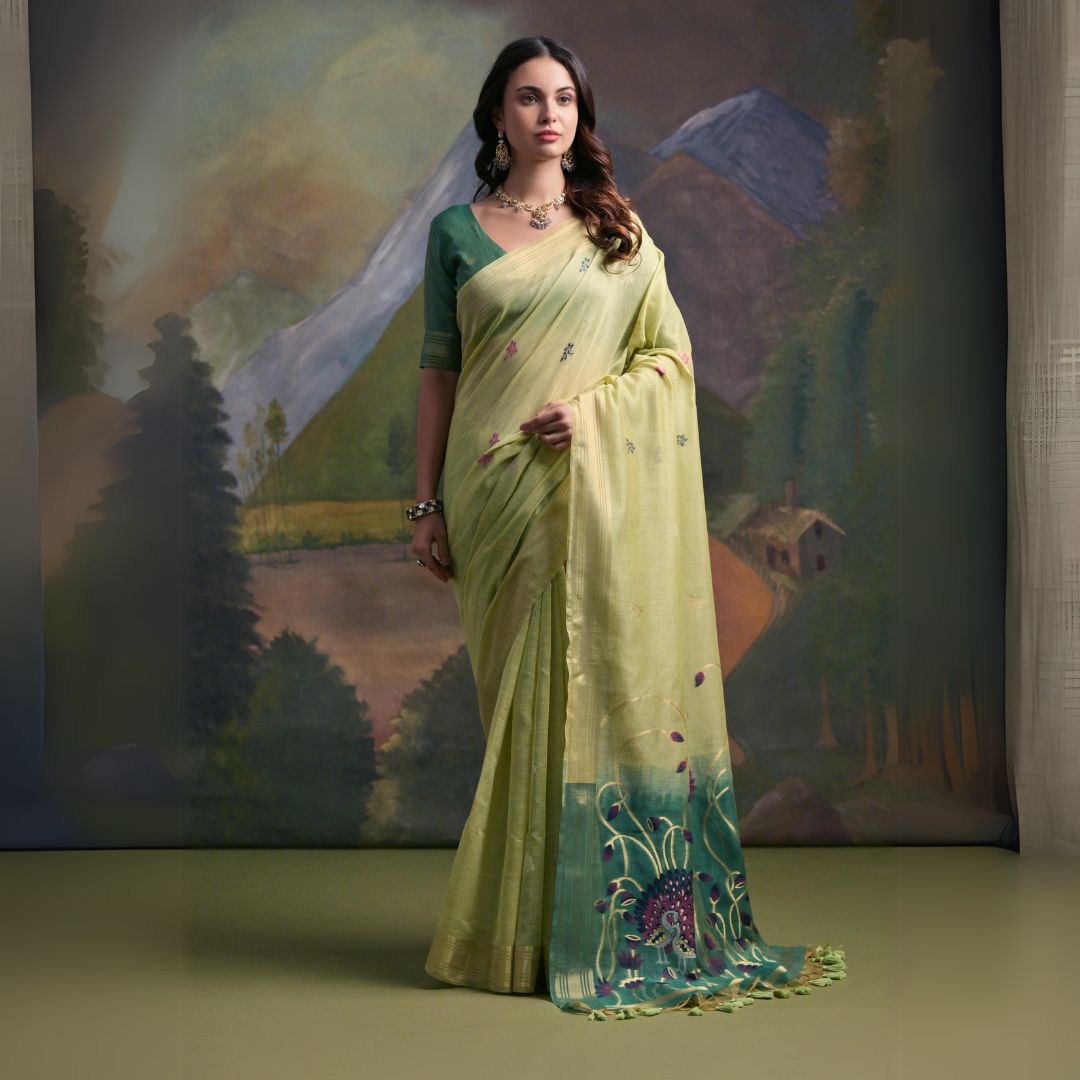 A woman models a soft Pista Green Muga Silk Saree with subtle Resham weaving. The pallu dramatically transitions to a deep teal color, featuring intricate purple and green floral/peacock Resham threadwork. She wears a teal blouse and an oxidized silver necklace.