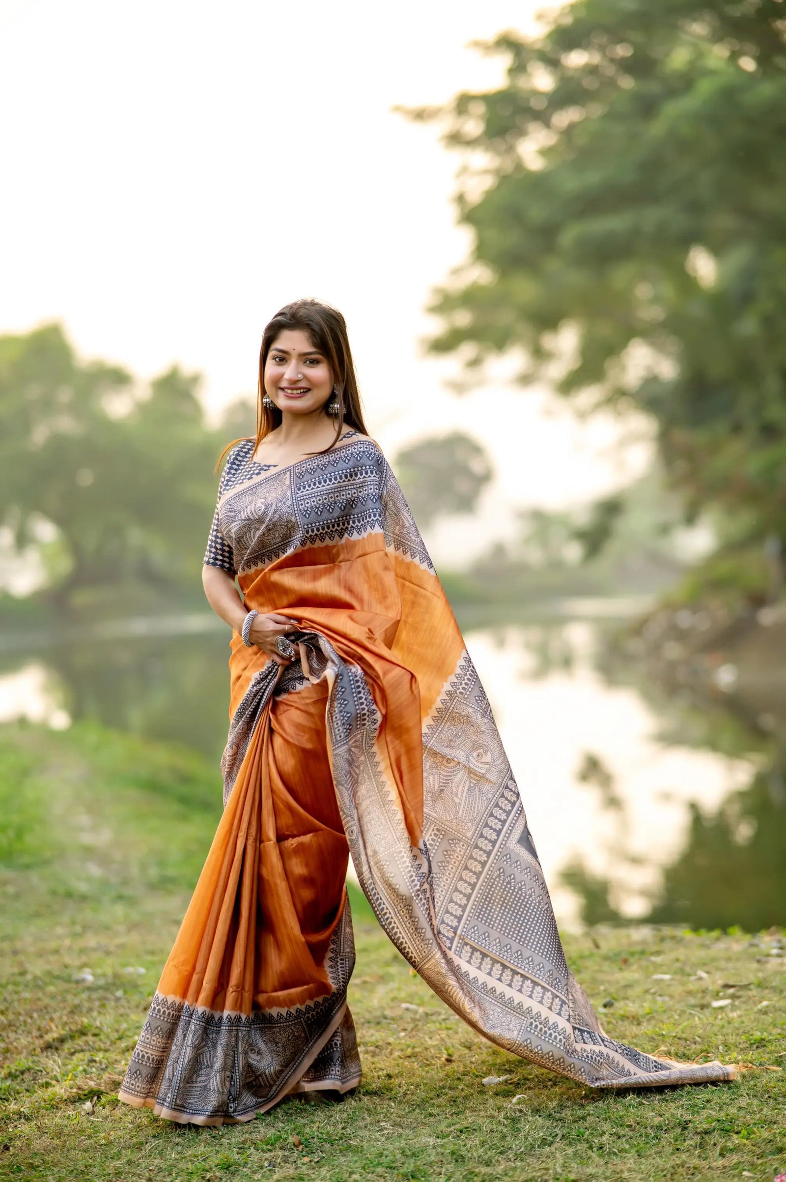 Woman wearing orange Madhubani print saree posing outdoors in traditional Indian attire