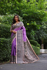 Woman wearing traditional purple Madhubani print saree with intricate designs and ethnic jewelry in a green outdoor setting
