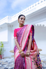 A woman models a vibrant Royal Purple Soft Silk Saree. The saree body features subtle woven patterns. It has a striking light pink contrast border with gold Zari. The pallu is a focal point, featuring rich, artistic Paithani-style print or weaving of colorful bird-on-branch motifs. She wears a fuchsia pink blouse and traditional gold jewelry, posing on an ornate white terrace.