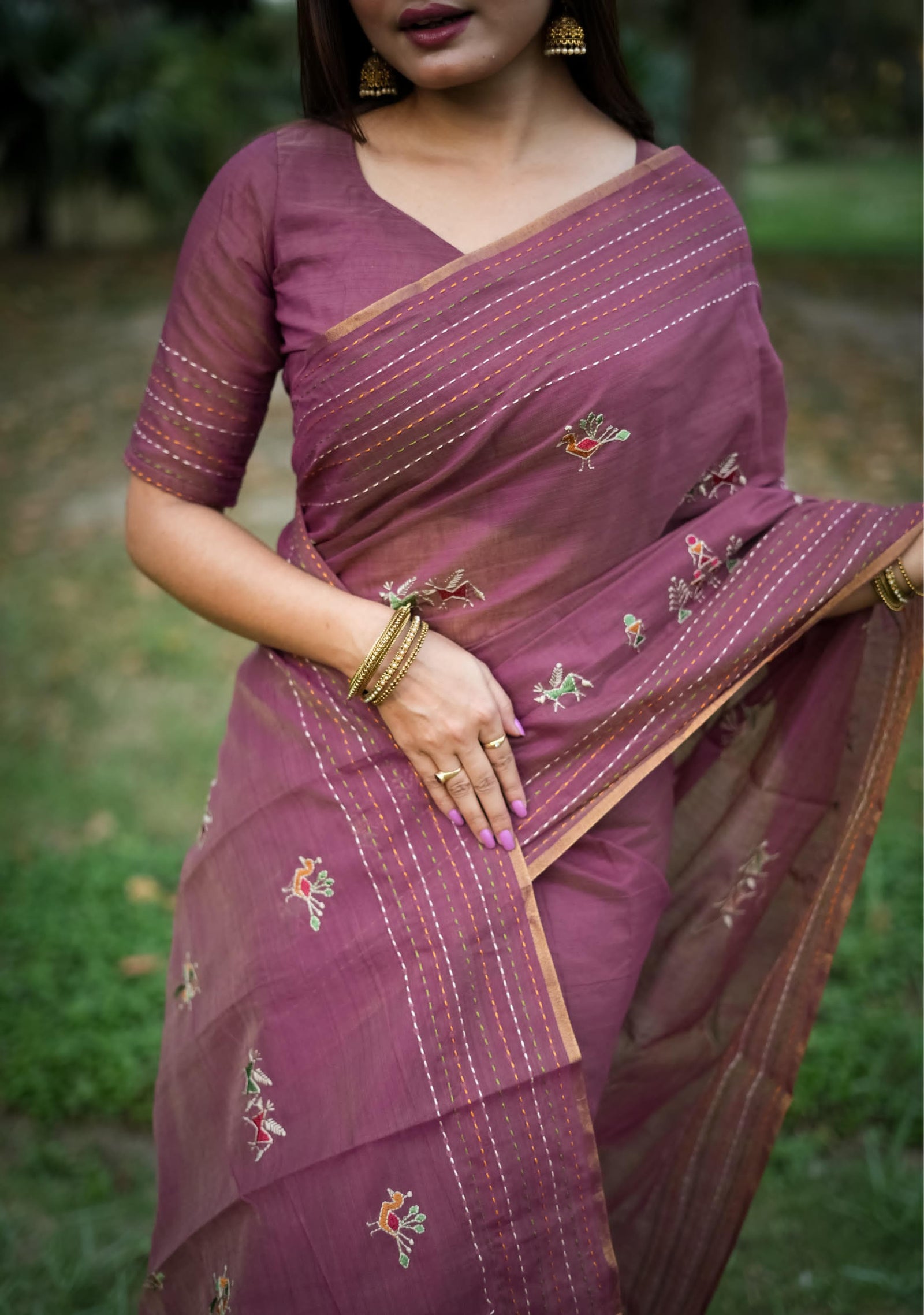 Woman in magenta traditional weaving saree with delicate motifs posing gracefully in a natural outdoor setting.