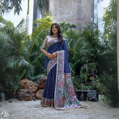 A woman models a deep Navy Blue Tussar Silk Saree with small scattered prints. The pallu features a wide, elaborate panel with intricate Madhubani-style folk art prints in white, red, green, and blue. She wears a cream/gold embellished blouse and a gold Kundan choker necklace.