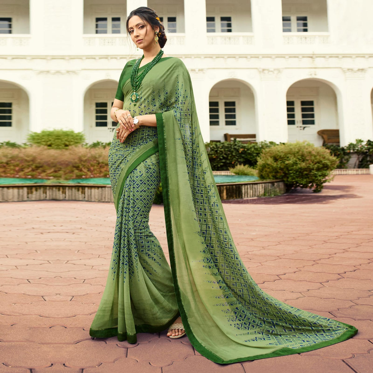 Woman in an olivine jacquard work saree with gold border standing indoors in an elegant room with arched decor and vintage furniture elements