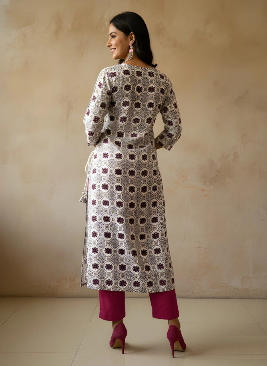 Woman wearing a patterned kurta with pink pants against a beige background