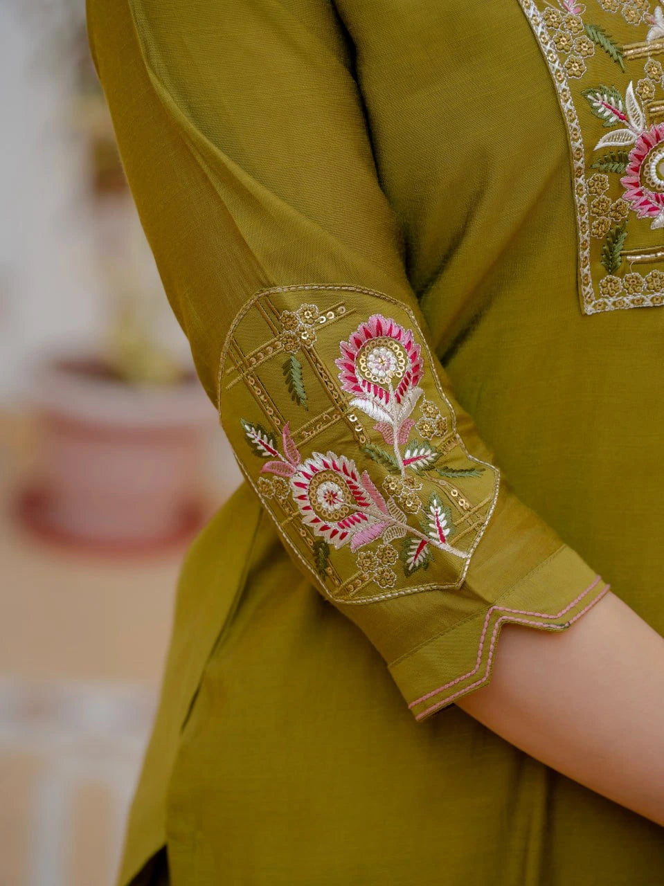 Green embroidered garment with floral patterns on a blurred background
