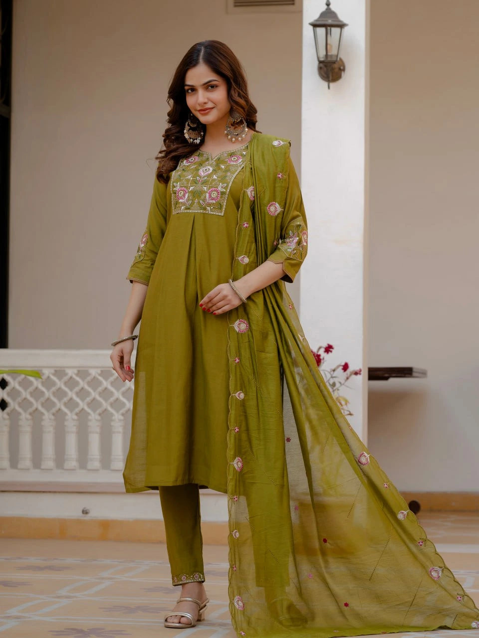 Woman wearing a green embroidered outfit with a dupatta in an indoor setting
