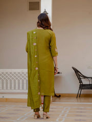 Woman wearing a green traditional outfit in a room with a chair and radiator.