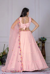 Woman wearing a pink traditional outfit with floral details in a decorated room.