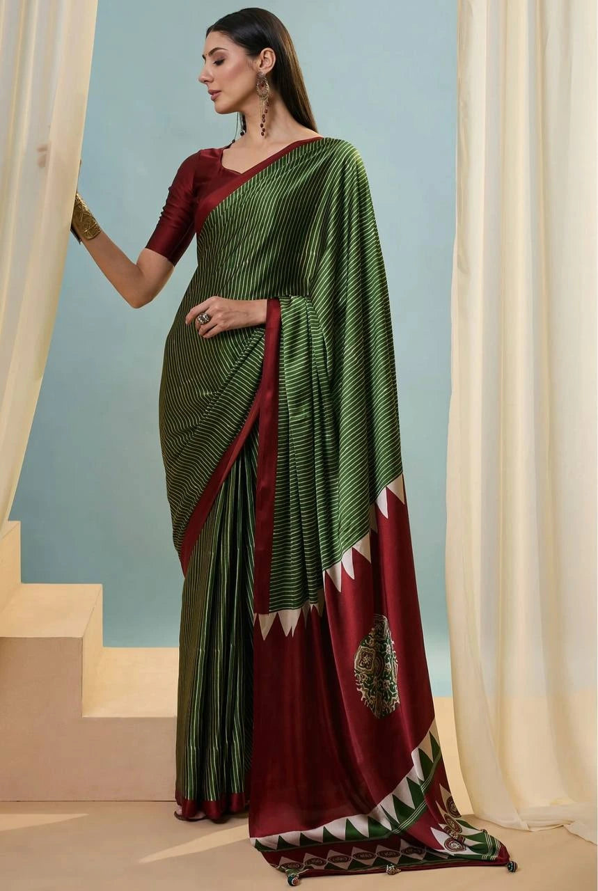 Woman wearing a green and red saree with a decorative border, standing against a light blue wall.