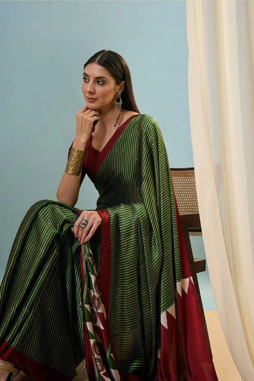 Woman in a green and red saree sitting on a chair against a light blue wall.