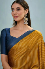 Woman wearing a yellow saree with a blue border and large earrings against a light gray background