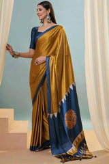 Woman wearing a traditional yellow and blue saree with a decorative pattern, standing against a light blue background.