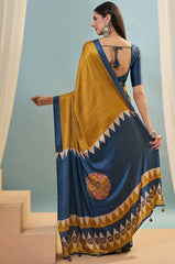 Woman wearing a blue and yellow saree with a geometric pattern, standing against a light blue wall.