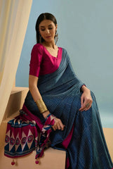 Woman in a blue saree with a pink blouse sitting on a bench against a light blue wall.