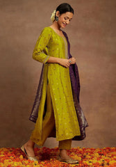 Woman in a green and purple traditional outfit standing on a floral ground with a brown background