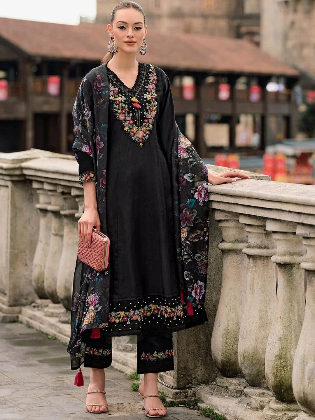 Woman in a black dress with floral embroidery standing on a stone bridge.