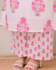 White outfit with pink floral patterns worn by a person on a wooden floor.