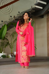 Woman in a bright pink traditional outfit with gold embroidery standing indoors.