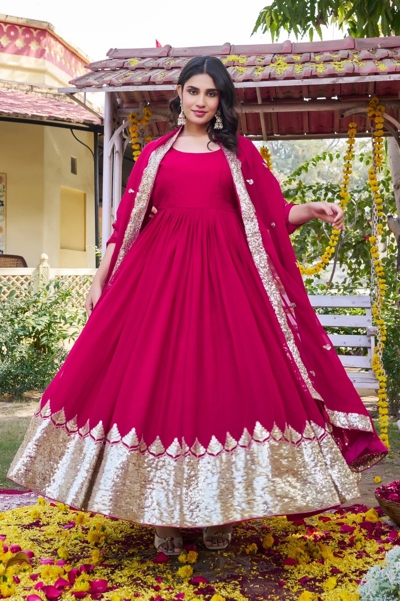 Woman in a pink and gold traditional outfit standing outdoors with greenery in the background