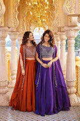 Two women in traditional orange and purple dresses standing in an ornate architectural setting.