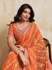 Woman wearing an orange and yellow saree with a beige background