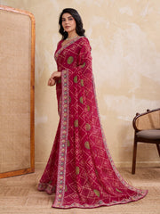 Woman wearing a red saree with intricate patterns in a room with a textured wall and chair.