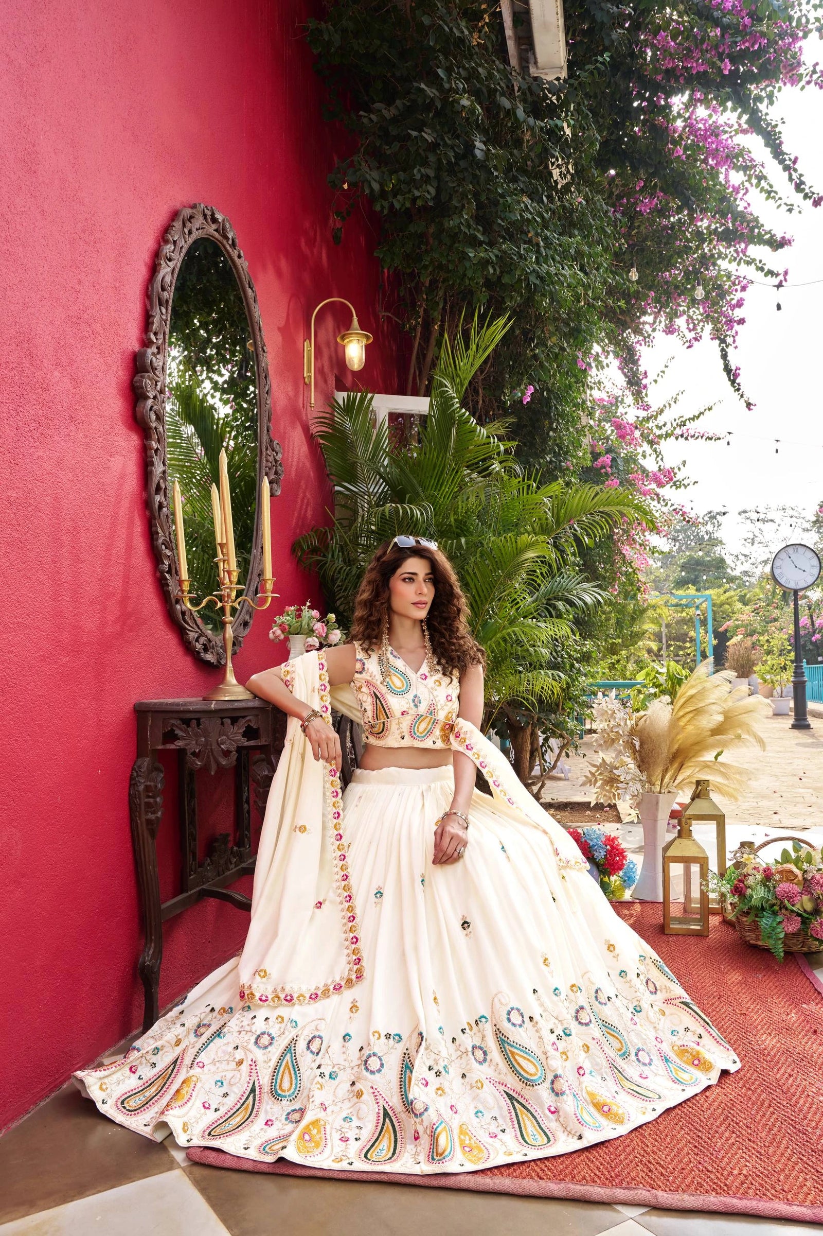 Woman in a traditional outfit standing against a red wall with decorative elements.