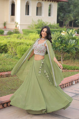 Woman in a green traditional outfit standing outdoors with greenery in the background