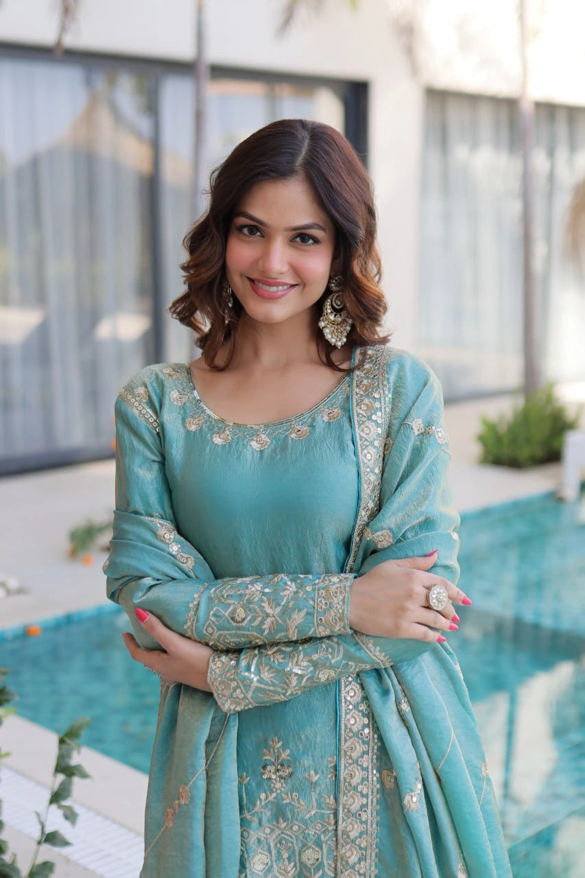 Woman wearing a teal traditional outfit with intricate patterns, standing outdoors.