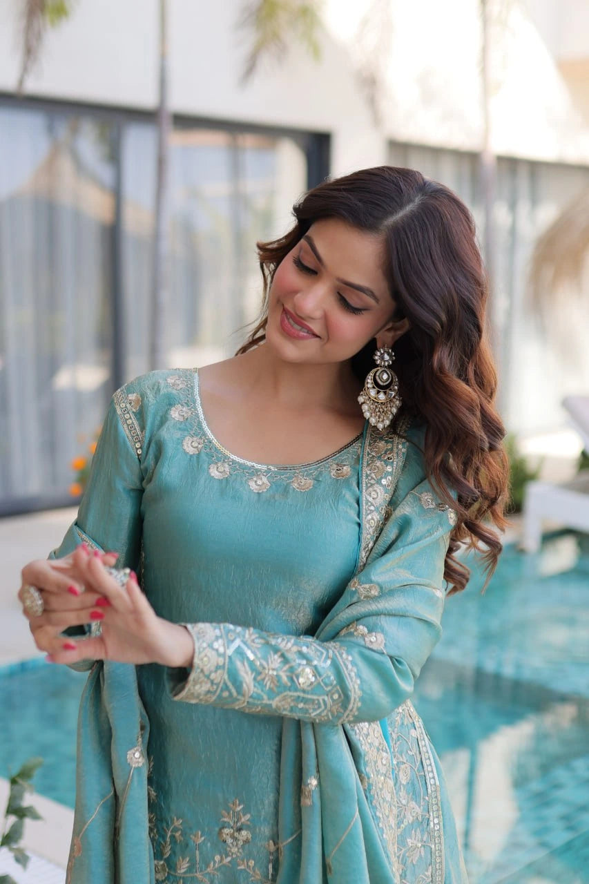 Woman in a teal traditional outfit with silver embroidery, standing outdoors.