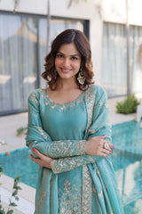 Woman wearing a teal traditional outfit with intricate patterns, standing outdoors.