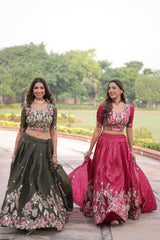 Two women in traditional outfits standing outdoors with greenery in the background