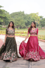 Two women in traditional outfits standing outdoors with greenery in the background