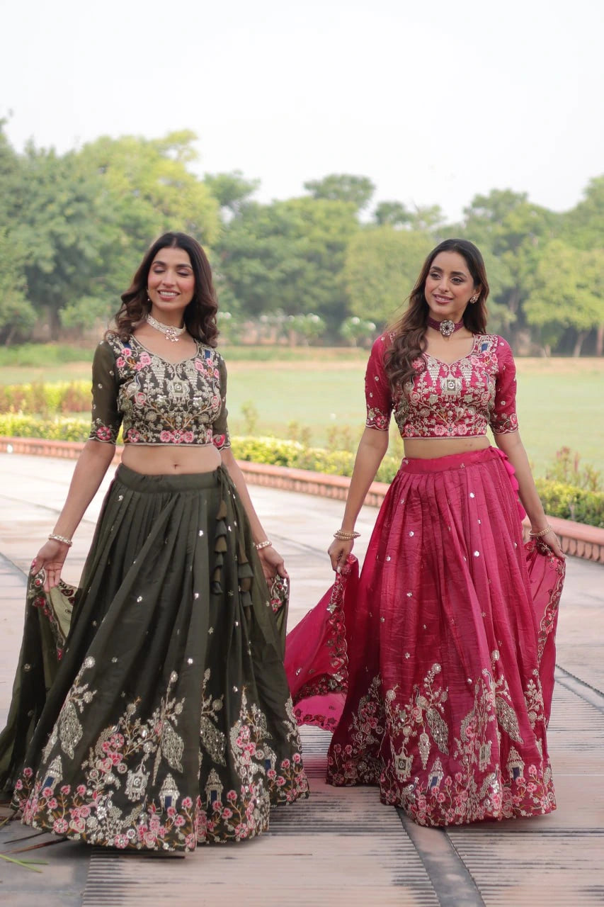 Two women in traditional outfits standing outdoors with greenery in the background