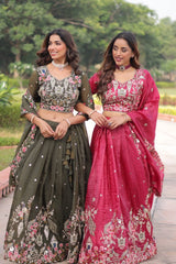 Two women in traditional outfits standing outdoors with greenery in the background