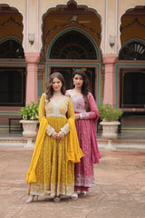Two women in traditional yellow and pink dresses standing in front of a decorative building.