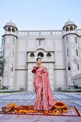 Woman in a pink saree standing in front of a building with decorative elements on the ground.