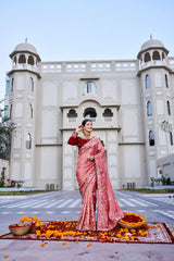 Woman in a pink saree standing in front of a white architectural building with decorative elements.