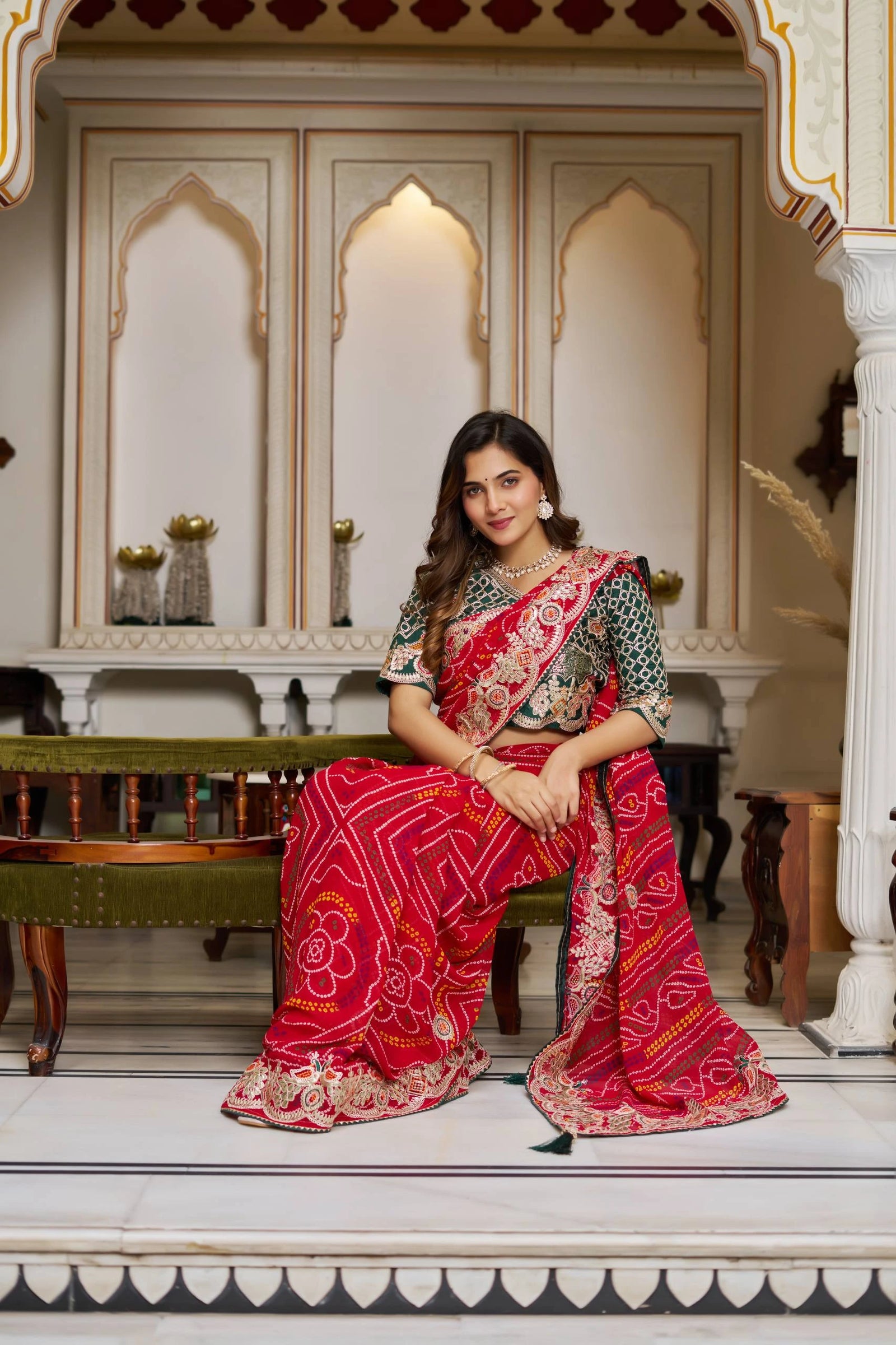 Woman in a traditional red and gold saree sitting in an ornate room.