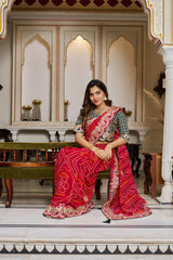 Woman in a traditional red and gold saree sitting in an ornate room.