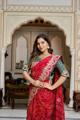Woman in a red saree with intricate patterns standing in an ornate architectural setting.
