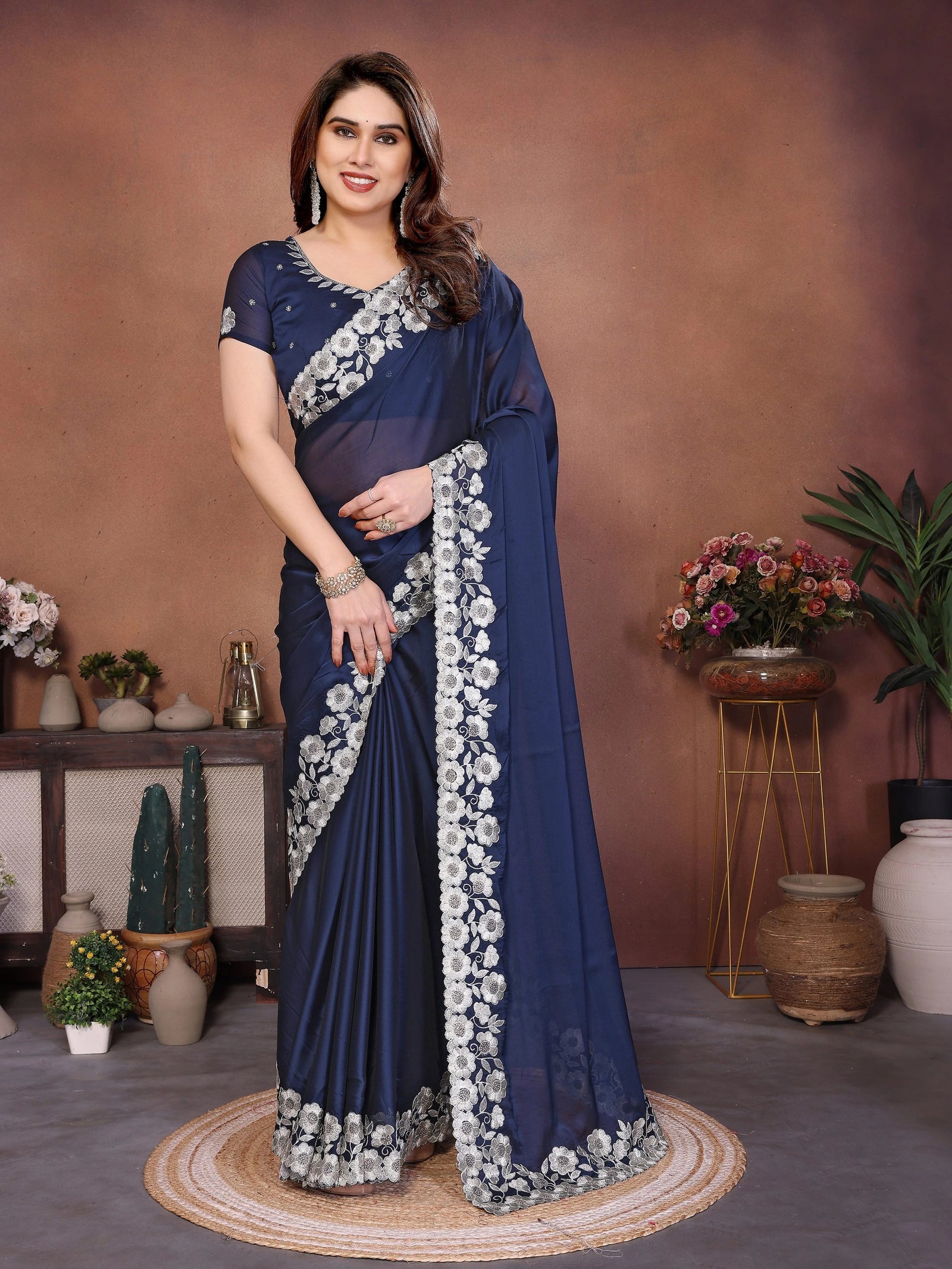 Woman in a blue saree with white floral patterns standing in a decorated room.