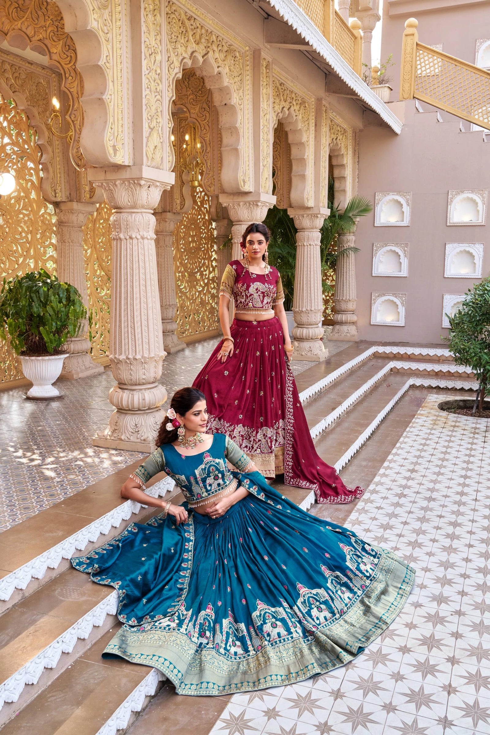 Two women in traditional Indian attire standing in an ornate indoor setting.