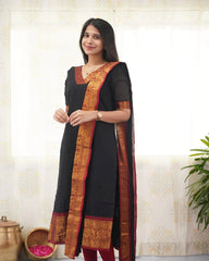 Woman wearing a black dress with orange and red border, standing against a light background.