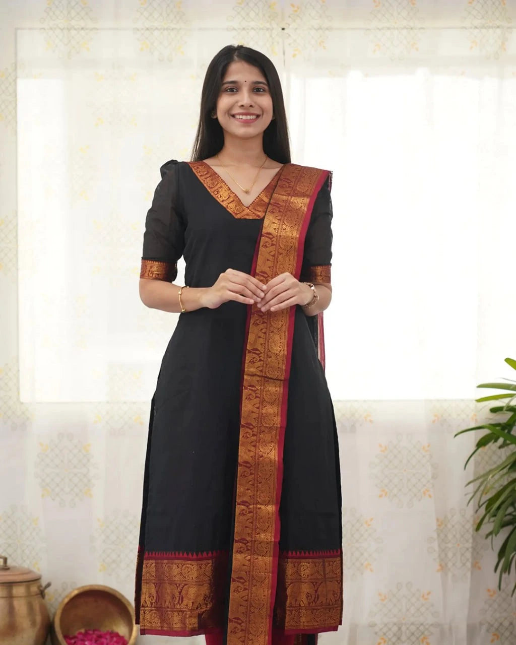Woman wearing a black traditional outfit with a decorative border indoors.