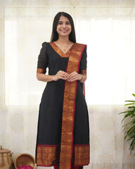 Woman wearing a black traditional outfit with a decorative border indoors.