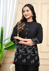Woman wearing a black top with white patterns, standing indoors.