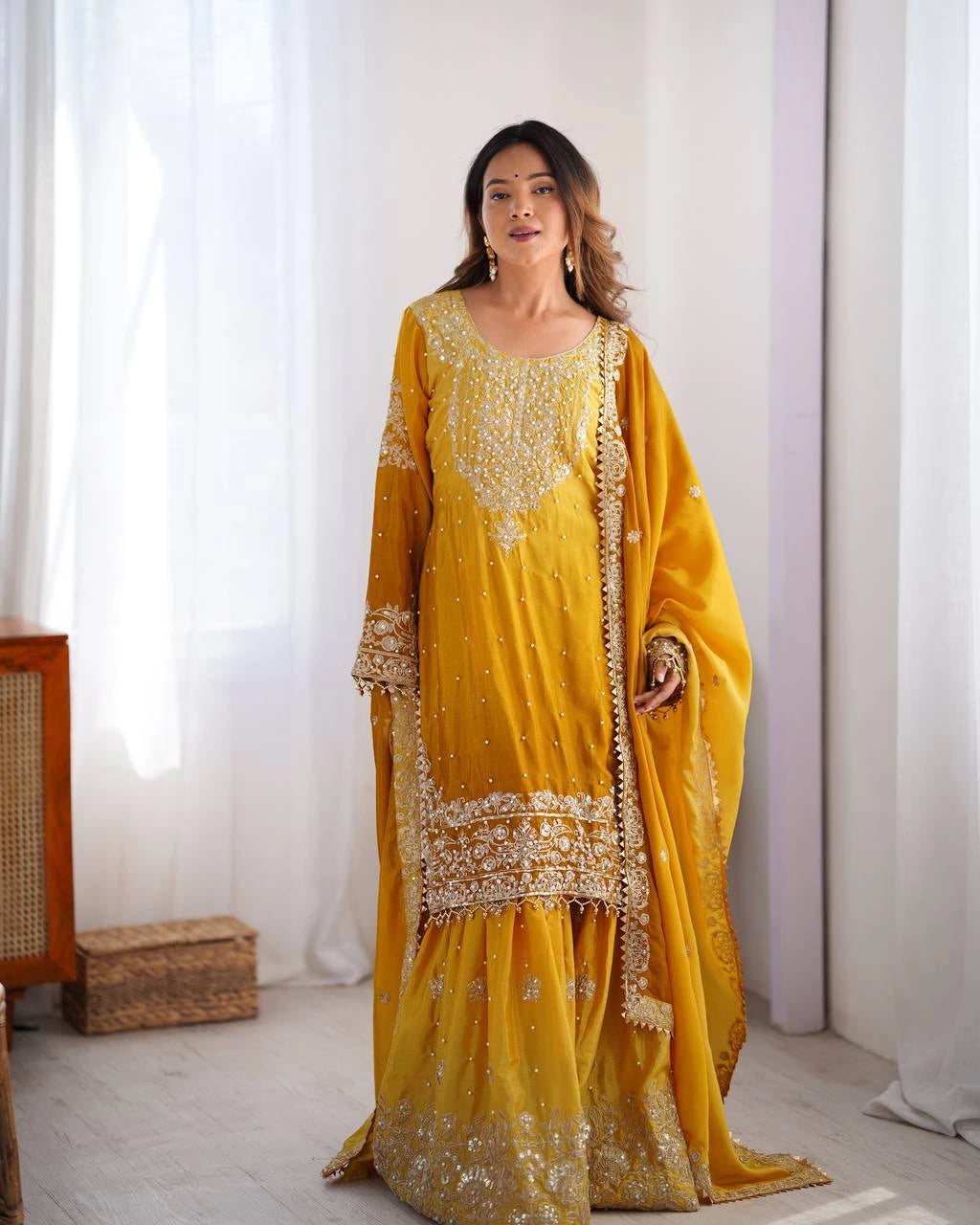 Woman in a yellow traditional outfit with gold embroidery standing in a bright room.
