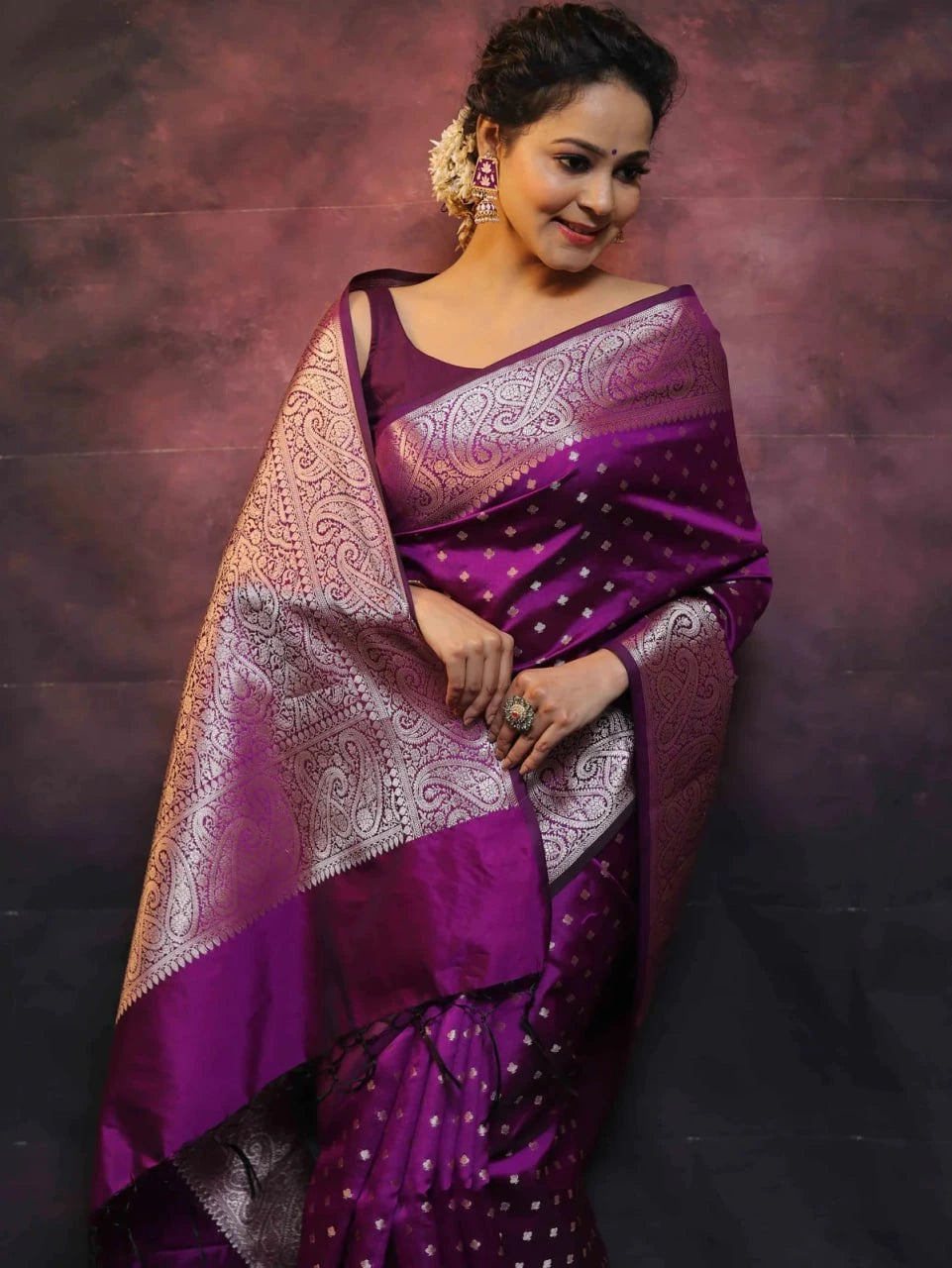 Woman wearing a purple saree with a patterned border against a dark background