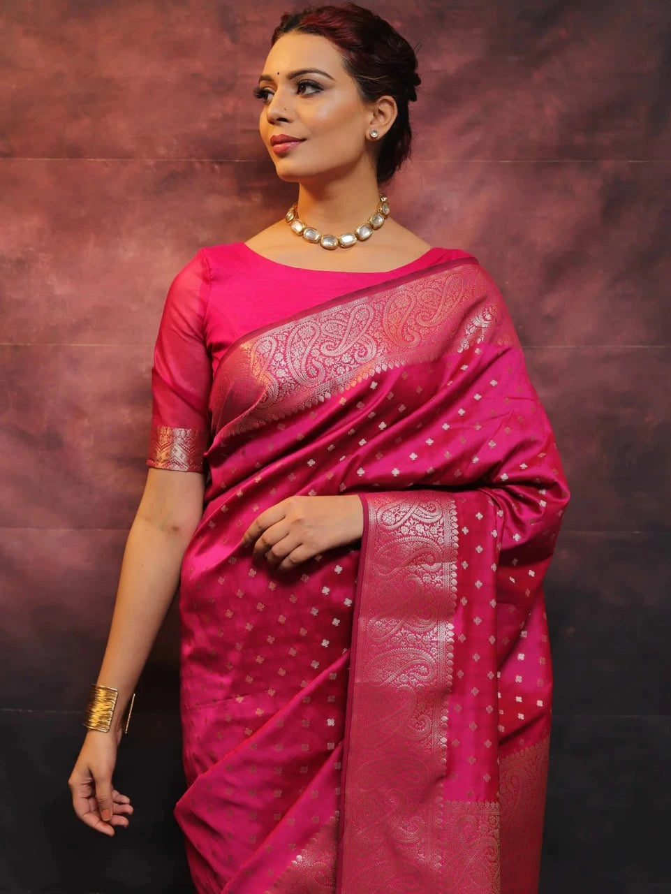 Woman wearing a pink saree with a patterned border against a dark background